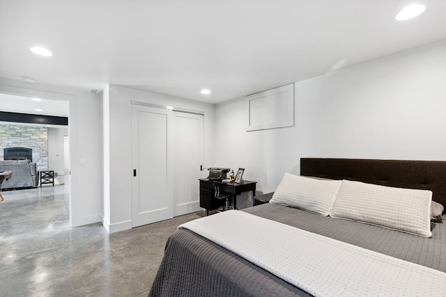 bedroom featuring baseboards, recessed lighting, concrete floors, a closet, and a stone fireplace
