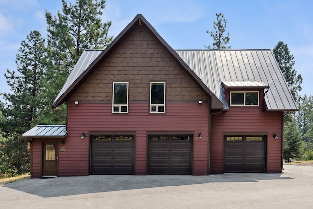 exterior space with a garage, a standing seam roof, metal roof, and aphalt driveway