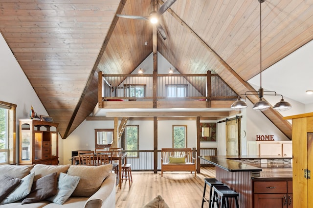 living area featuring a barn door, light wood-style floors, beamed ceiling, ceiling fan, and wooden ceiling