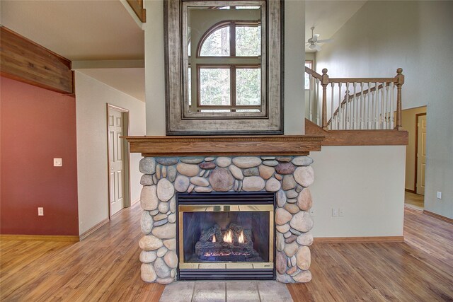 details with wood finished floors, a ceiling fan, baseboards, and a stone fireplace