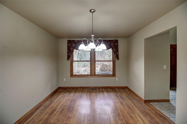 unfurnished room with light wood-style flooring, baseboards, and a chandelier
