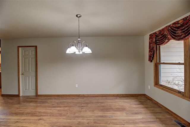 spare room with baseboards, a notable chandelier, visible vents, and light wood-type flooring