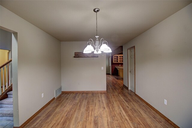 unfurnished dining area with wood finished floors, stairs, a chandelier, baseboards, and visible vents