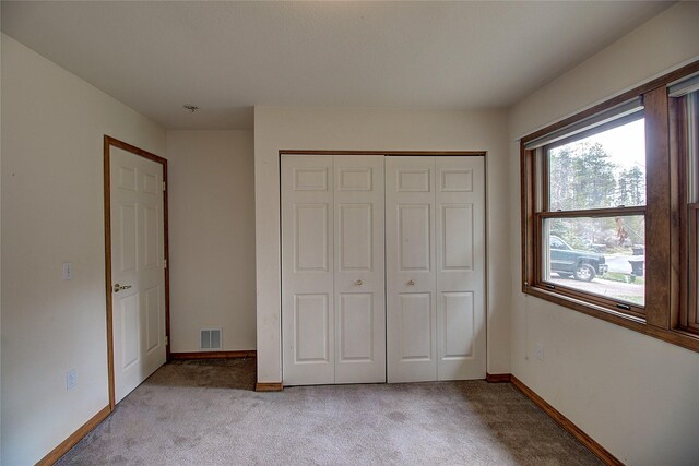 unfurnished bedroom featuring light colored carpet, baseboards, visible vents, and a closet