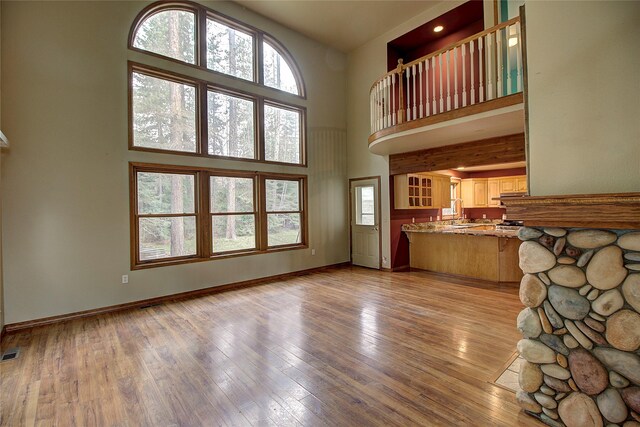 unfurnished living room featuring light wood-style floors, visible vents, a towering ceiling, and baseboards