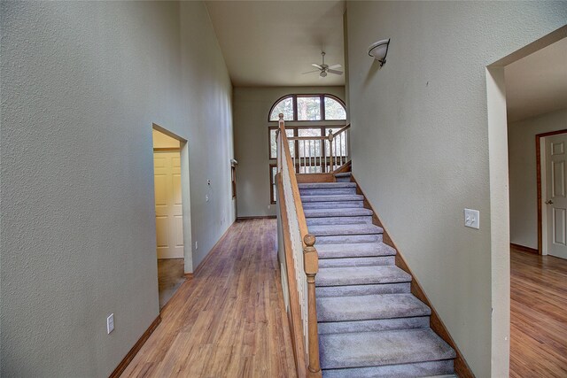 stairway featuring a textured wall, a ceiling fan, and wood finished floors