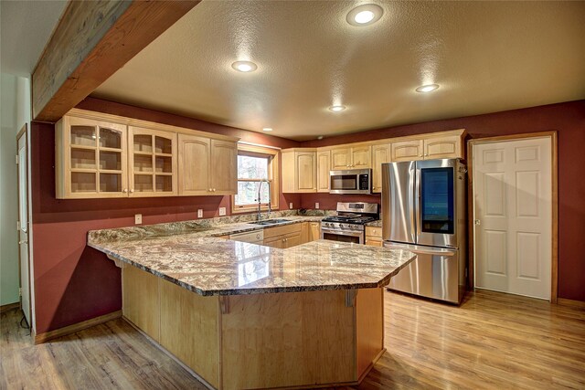 kitchen with a peninsula, light wood-style floors, glass insert cabinets, light stone countertops, and appliances with stainless steel finishes