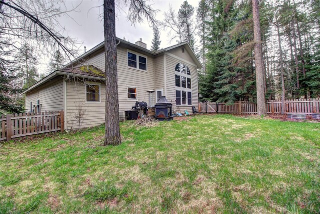 back of house with a yard, a fenced backyard, and a chimney