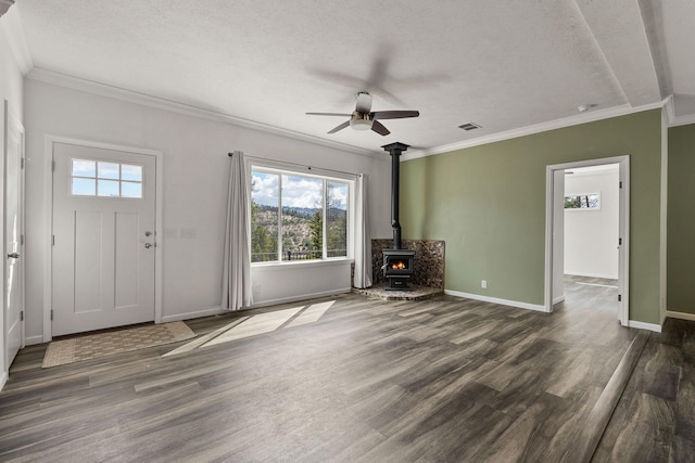 unfurnished living room with ceiling fan, visible vents, a wealth of natural light, and a wood stove