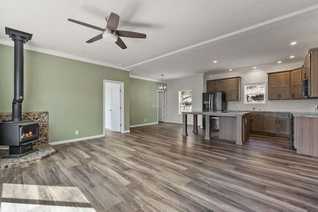 unfurnished living room featuring dark wood-style floors, baseboards, ceiling fan, crown molding, and a wood stove