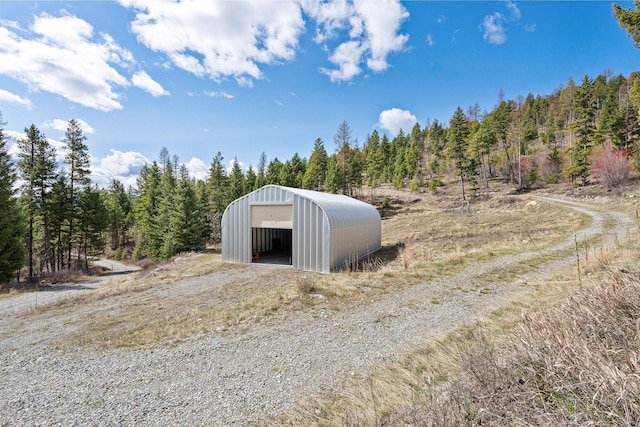 view of pole building with dirt driveway and a view of trees