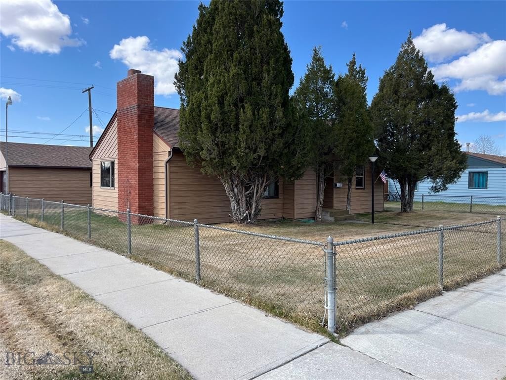 view of front of home with a chimney, roof with shingles, a front yard, and a fenced front yard