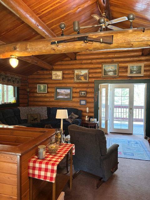 carpeted living area featuring vaulted ceiling with beams, log walls, wood ceiling, and a ceiling fan