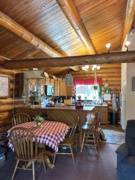 dining space featuring lofted ceiling with beams, log walls, and wooden ceiling