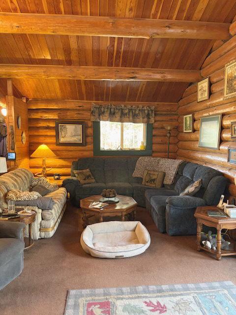 carpeted living room with wooden ceiling, rustic walls, and beamed ceiling