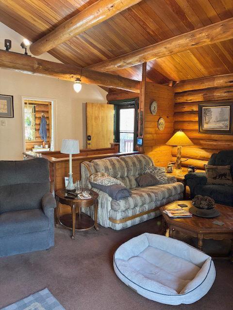 carpeted living room with wooden ceiling, beam ceiling, and rustic walls