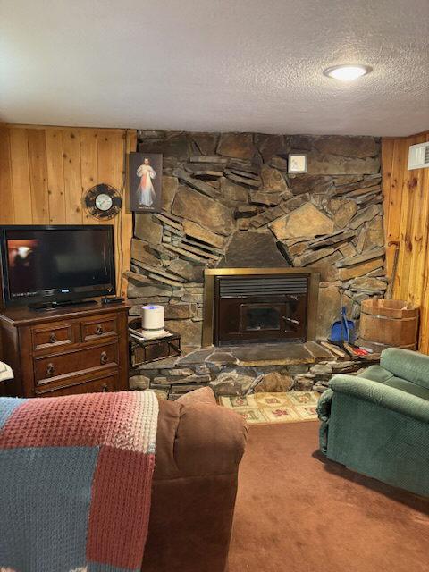 carpeted living room featuring a stone fireplace, a textured ceiling, and wooden walls