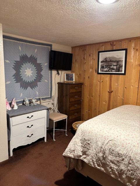 2025 Emmons Canyon Rd, Kila, MT 59920 - bedroom featuring dark colored carpet, wood walls, and a textured ceiling