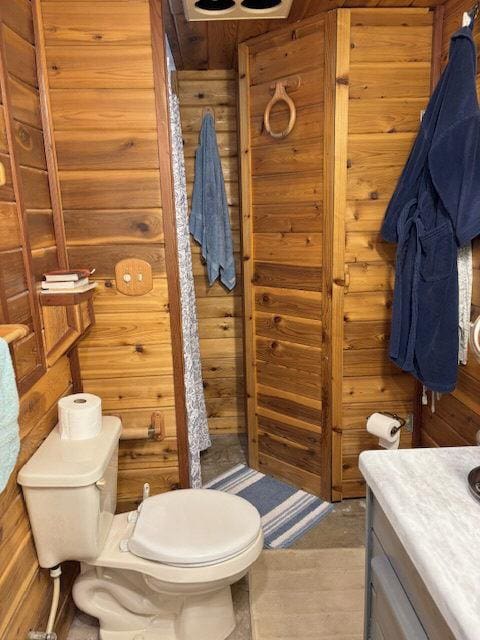 bathroom with toilet, vanity, and wood walls