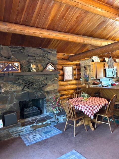 carpeted dining area with a fireplace, log walls, wood ceiling, and lofted ceiling with beams