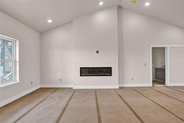 unfurnished living room with recessed lighting, a glass covered fireplace, baseboards, and high vaulted ceiling