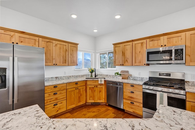 kitchen with stainless steel appliances, a sink, dark wood-type flooring, and light stone counters