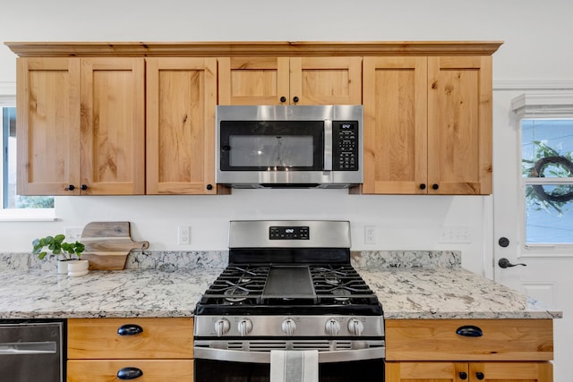 kitchen featuring stainless steel appliances, light brown cabinets, and light stone counters