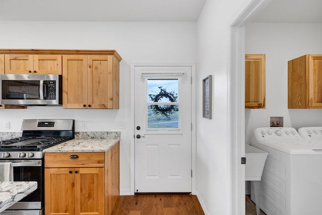 kitchen featuring washing machine and dryer, light stone countertops, appliances with stainless steel finishes, and dark wood-style flooring