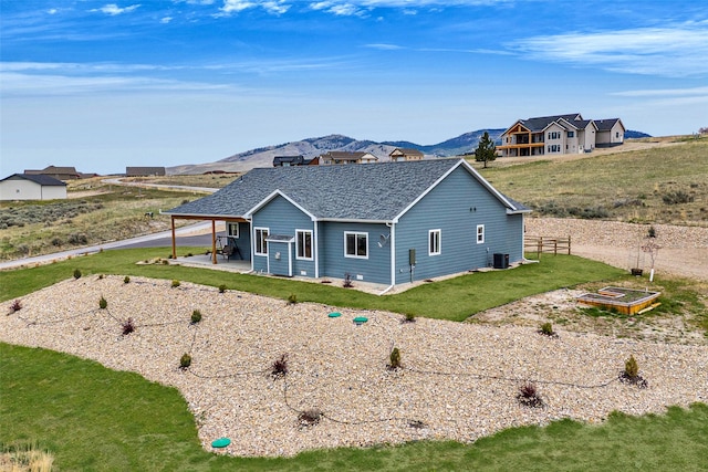 back of property with a shingled roof, a yard, central air condition unit, a patio, and a mountain view