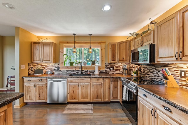 kitchen with a sink, stainless steel appliances, decorative light fixtures, backsplash, and dark wood-type flooring