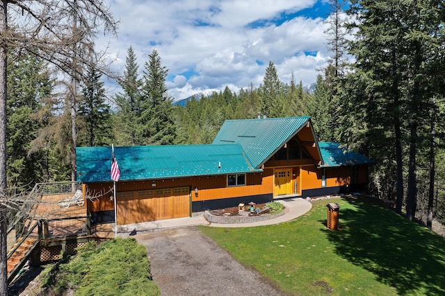 view of front of property featuring a forest view, aphalt driveway, a front yard, and metal roof