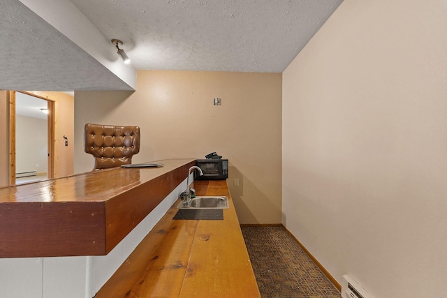 interior space featuring a baseboard radiator, a textured ceiling, baseboards, and a sink