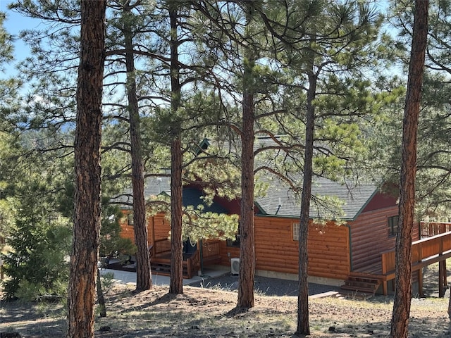 view of side of home with log veneer siding, a shingled roof, and a deck