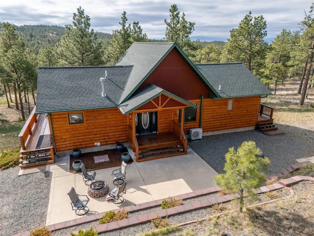view of front facade with a patio, a view of trees, roof with shingles, and an outdoor fire pit