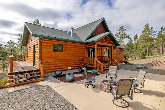 rear view of house featuring a deck, faux log siding, an outdoor fire pit, a patio, and a shingled roof