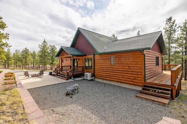 exterior space with a deck, a patio, faux log siding, a shingled roof, and ac unit