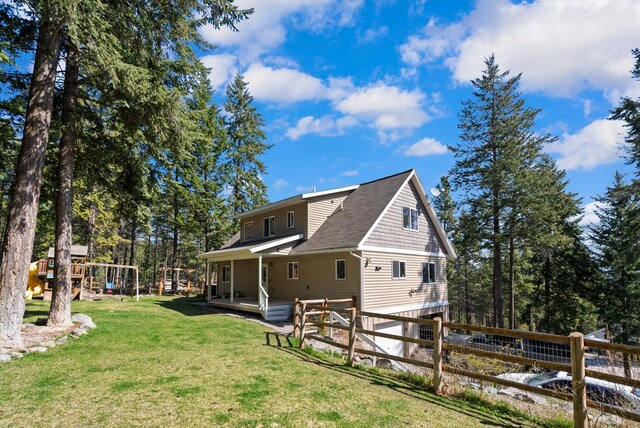 exterior space with fence, a yard, a shingled roof, and a playground