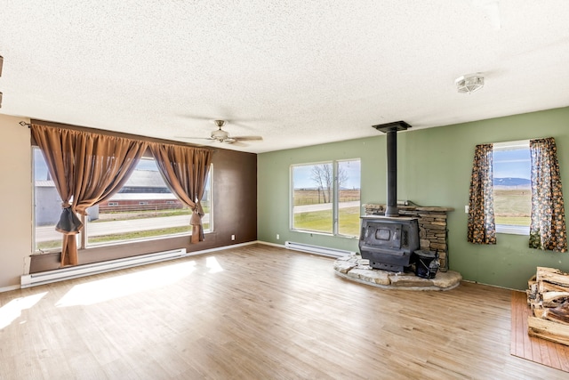 unfurnished living room featuring a baseboard radiator, baseboard heating, ceiling fan, a wood stove, and a textured ceiling