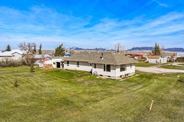 back of house with a mountain view, a lawn, and a shingled roof