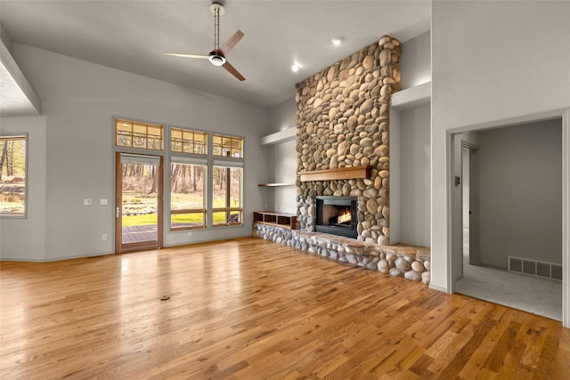 unfurnished living room with visible vents, a wealth of natural light, wood finished floors, a ceiling fan, and a stone fireplace