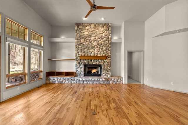 unfurnished living room with a high ceiling, a ceiling fan, a stone fireplace, and wood finished floors