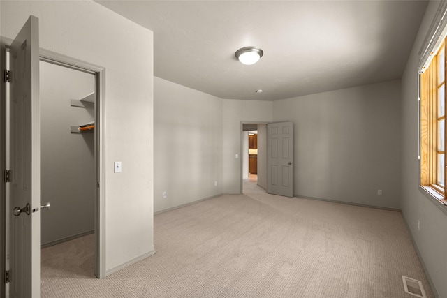 unfurnished bedroom with a walk in closet, visible vents, light colored carpet, and baseboards