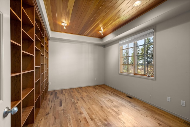 empty room featuring wood ceiling, visible vents, a tray ceiling, baseboards, and wood finished floors