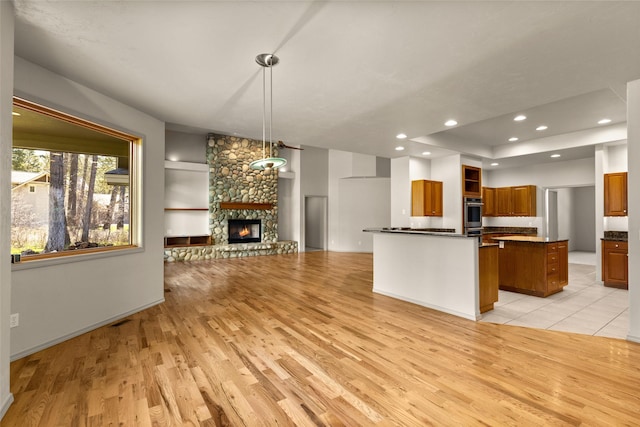 kitchen with brown cabinets, dark countertops, open floor plan, light wood finished floors, and a stone fireplace