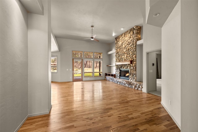 unfurnished living room with a ceiling fan, baseboards, wood finished floors, and a fireplace
