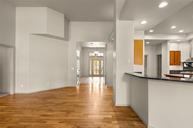 kitchen with wall chimney range hood, brown cabinets, baseboards, light wood-type flooring, and recessed lighting
