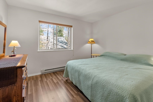 bedroom featuring wood finished floors, a baseboard heating unit, and baseboards