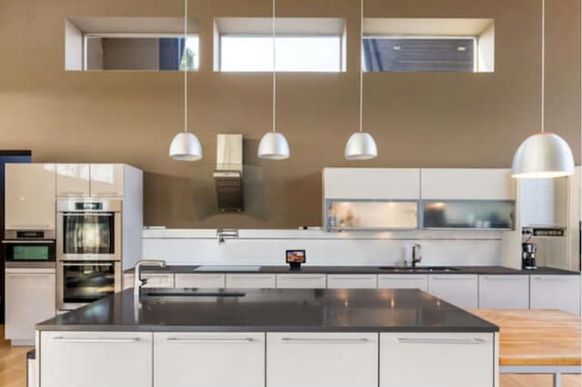 kitchen with a sink, double oven, dark countertops, ventilation hood, and white cabinets