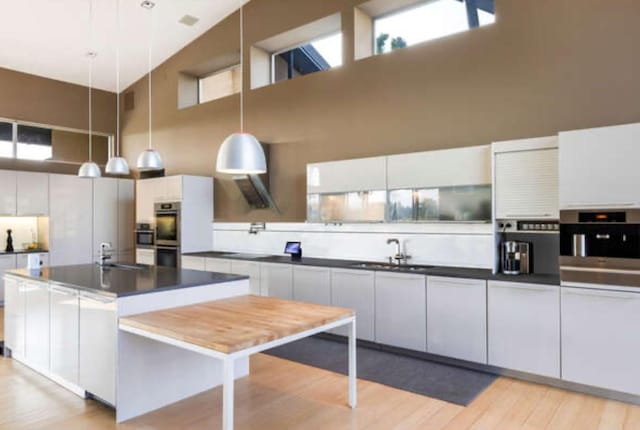 kitchen featuring a sink, dark countertops, a high ceiling, light wood-style flooring, and pendant lighting
