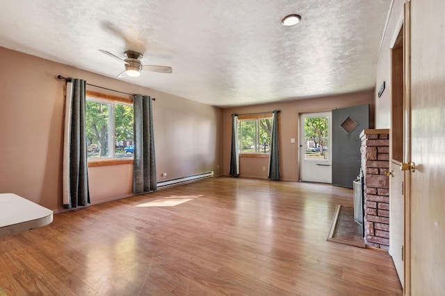 unfurnished living room featuring a baseboard heating unit, light wood finished floors, a textured ceiling, and ceiling fan